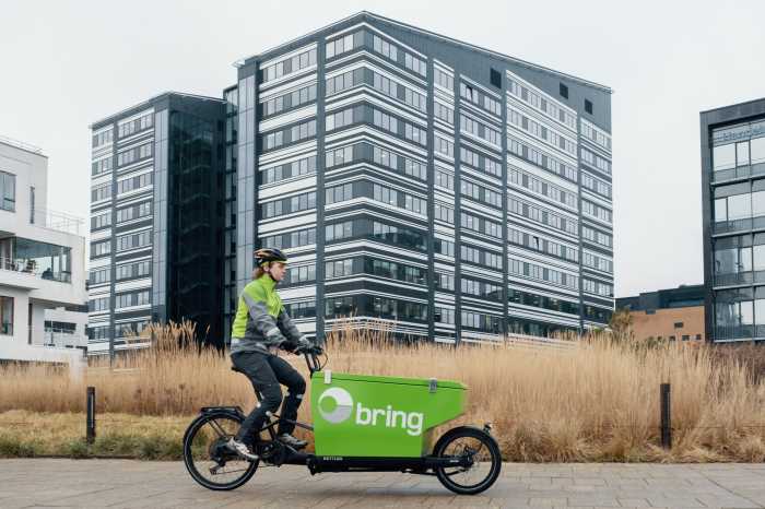 Bringbud på grøn elcykel transporterer pakker i et boligområde.