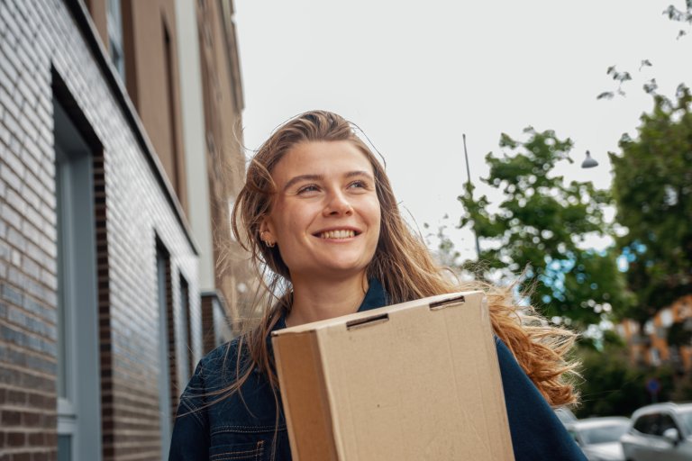 En smilende kvinde står med en pakke i hånden