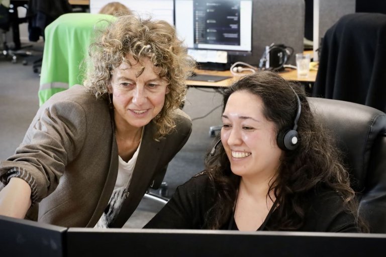 En kvinde som hjælper en kvindelig kollega foran en computerskærm