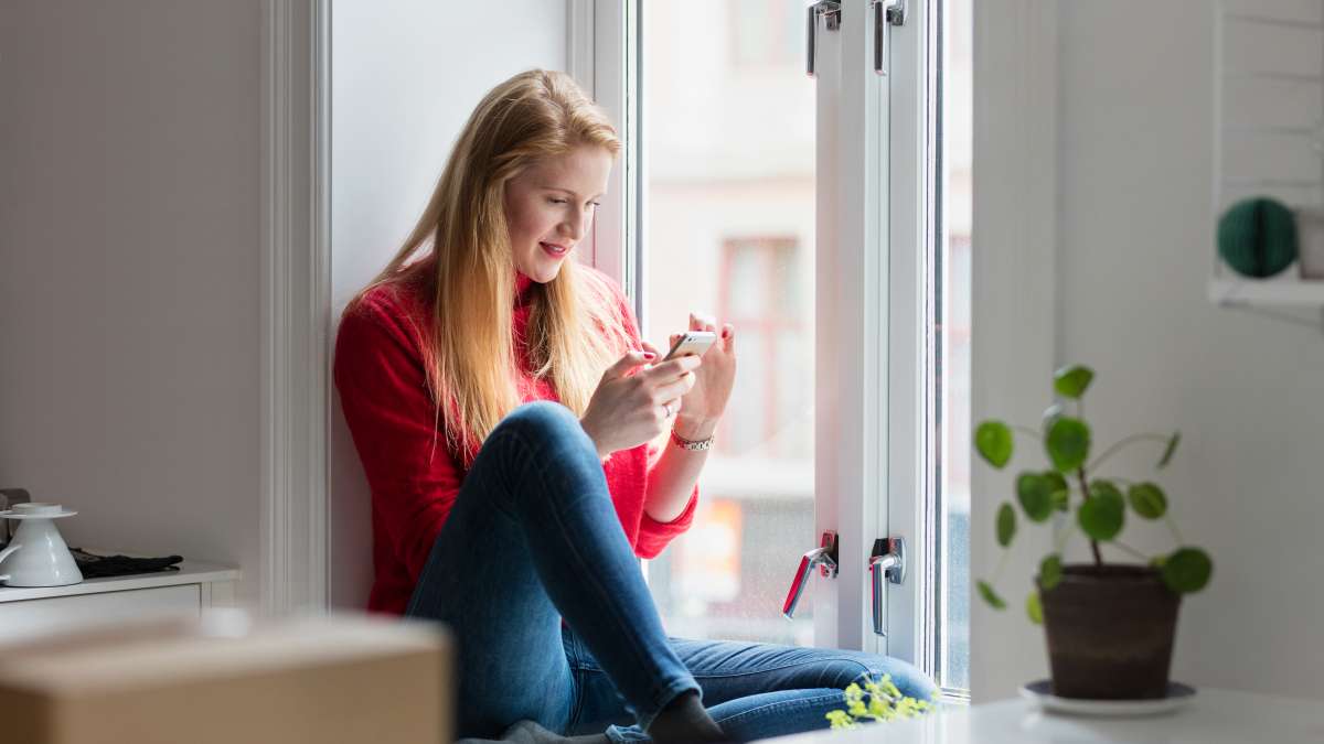 Kvinde sidder i et vindue med en mobiltelefon